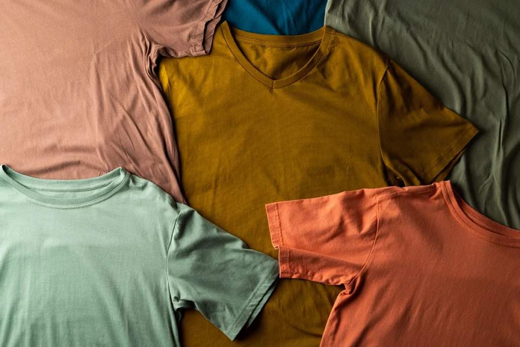 Flat lay of fall-colored t-shirts in earthy tones of orange, mustard, green, and brown, ideal for custom screen printing designs.
