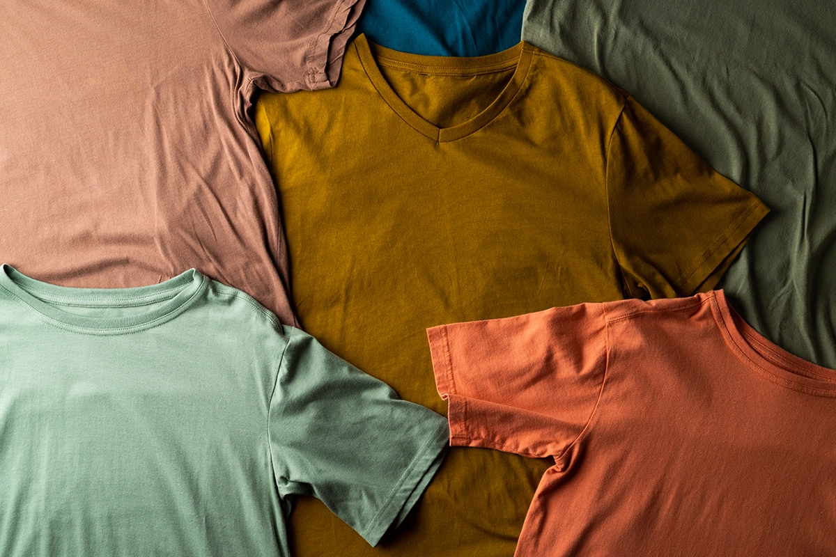 Flat lay of fall-colored t-shirts in earthy tones of orange, mustard, green, and brown, ideal for custom screen printing designs.