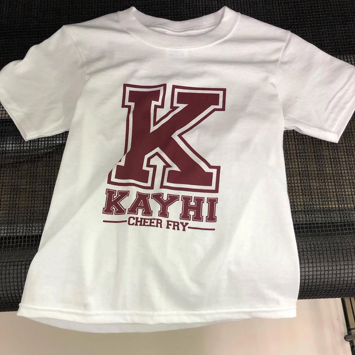 White T-shirt with maroon lettering that reads “KAYHI Cheer Fry” featuring a large varsity-style K on the front.