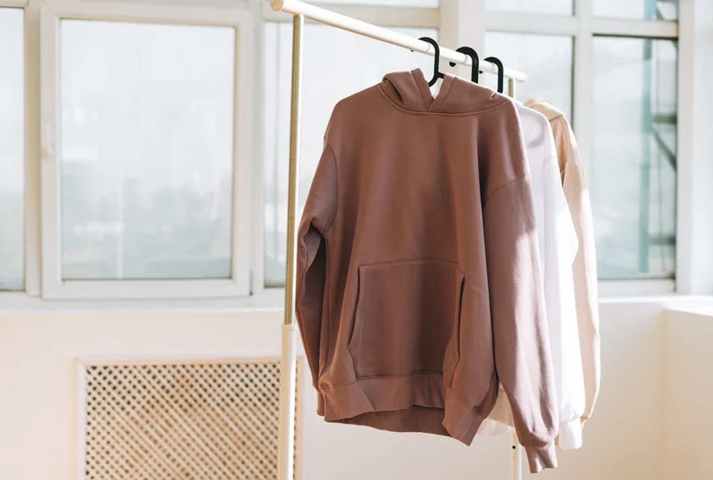 Neutral-toned hoodies hanging neatly on a rack in a bright studio, showcasing minimalist modern fashion.