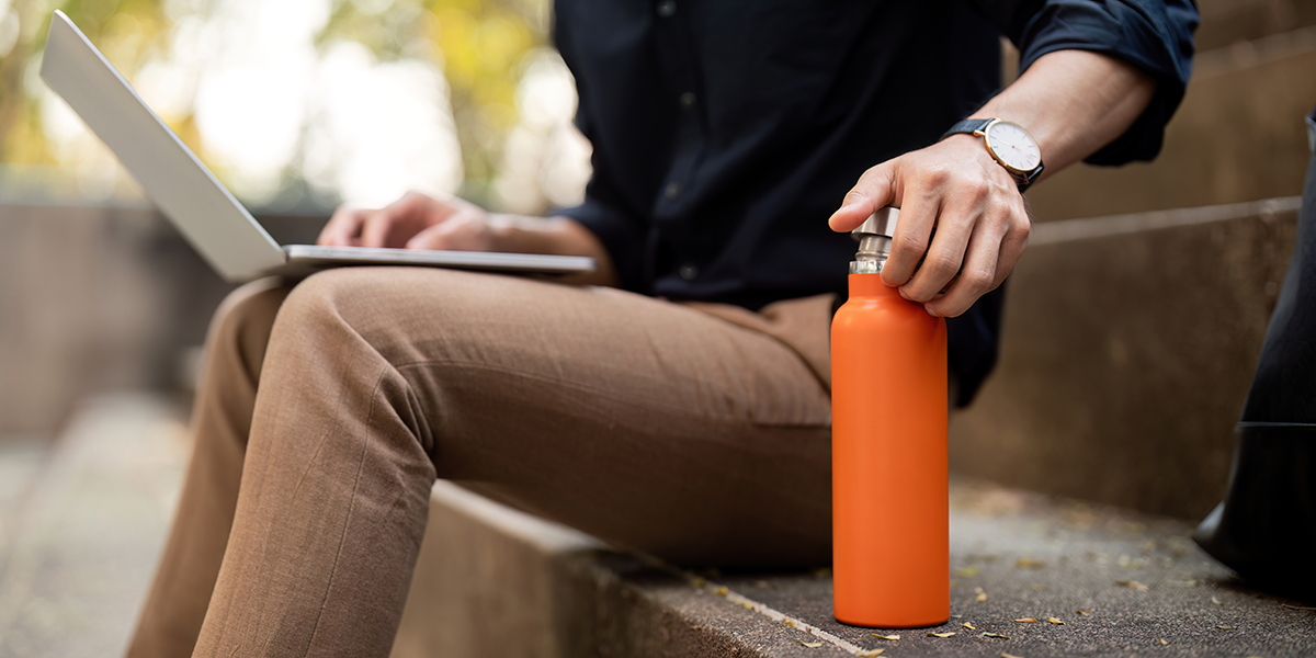 Business professional sitting outdoors with a laptop and reusable water bottle, representing branded drinkware for everyday use.
