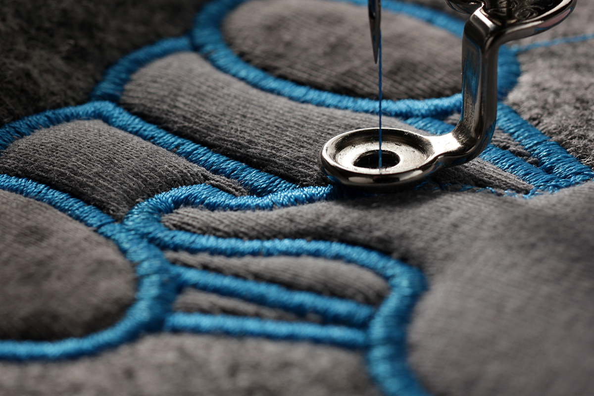 Macro view of an embroidery needle stitching blue thread into fabric, highlighting precision embroidery detail.