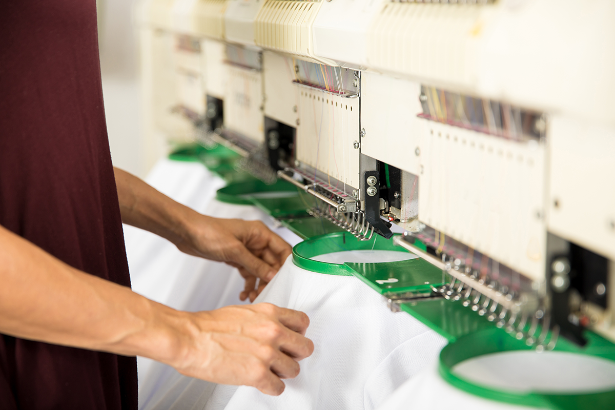 Commercial embroidery machine stitching fabric hoops in a production setting, representing professional apparel embroidery services.