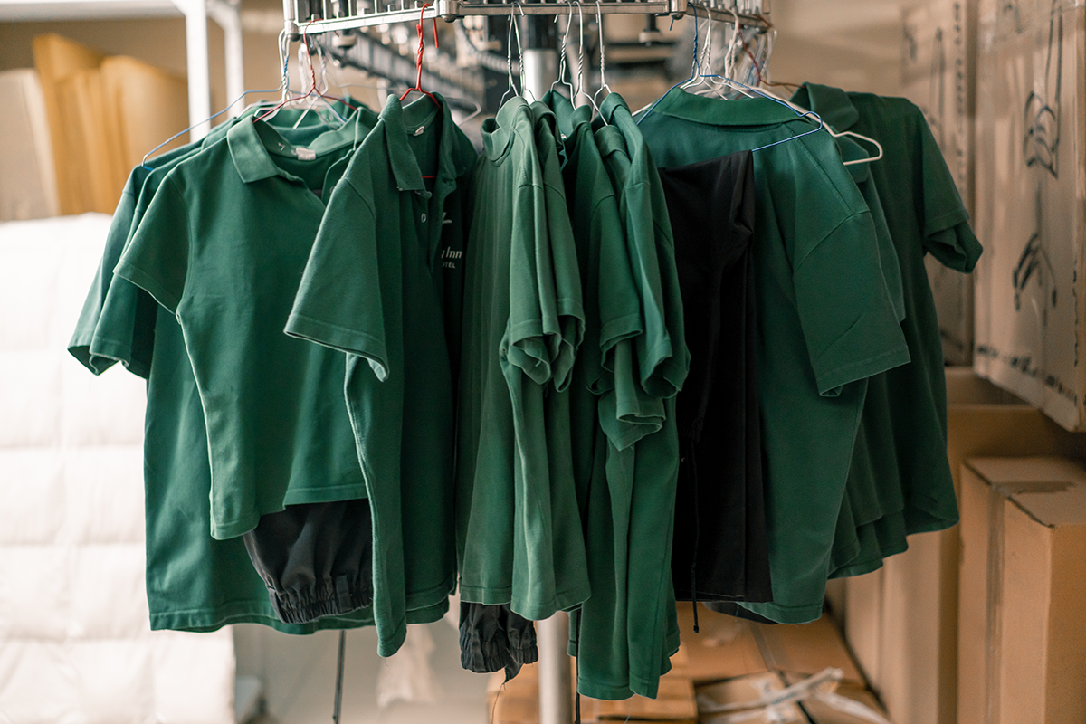 Rack of green company uniforms hanging in an industrial laundry or production area, representing professional workwear and uniform services.