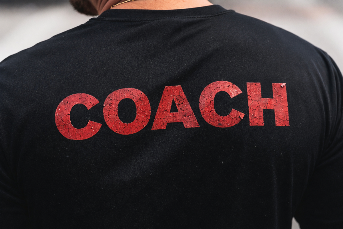 Close up of a black shirt with cracked and worn heat transfer lettering, representing aged apparel graphics and repeated washing.