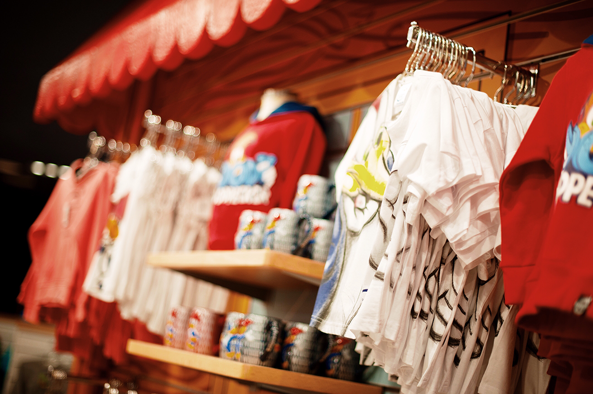 Colorful souvenir shop display with graphic t-shirts, mugs, and hanging apparel inside retail store
